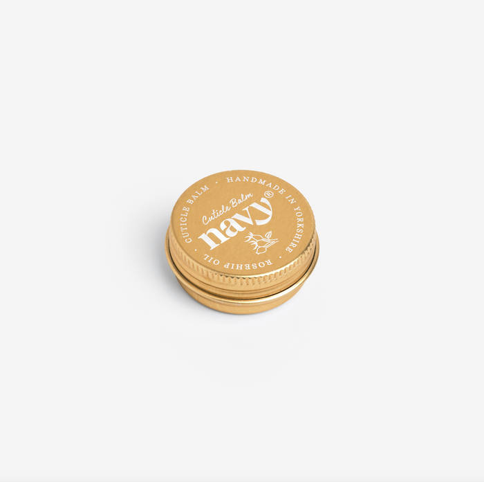 A gold-colored metal tin of Navy brand Cuticle Balm, lid on, with product details visible on the lid.