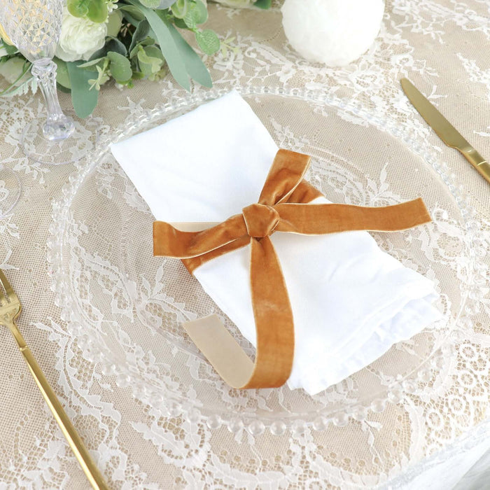White napkin with brown velvet ribbon on a decorative plate.
