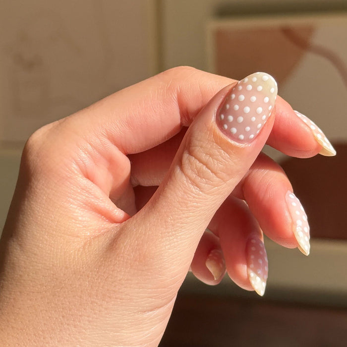 Hand with almond-shaped nails featuring white polka dots on neutral base showcasing Polka Dot Mani Polish Set manicure