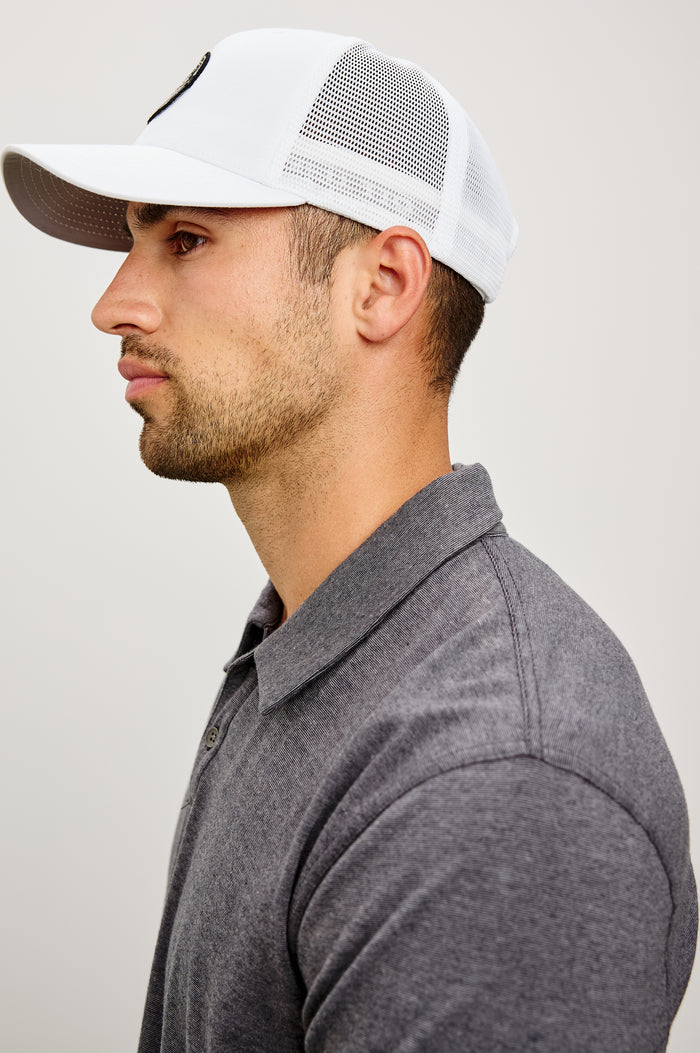 Golf Hat With Embroidered Branded Patch at Front, Adjustable Snapback, Mesh Back, and 6-Panel Construction in White Colorway - Upper Body Side View Featured on Model