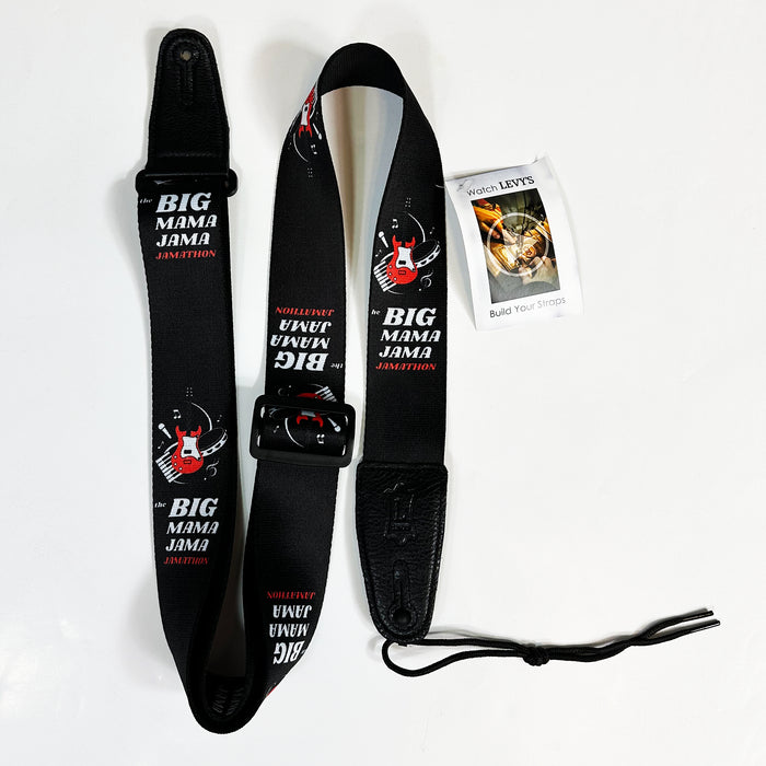 A black guitar strap by Steve Vai featuring red guitar graphics and the text "BIG MAMA JAMA JAMITION," inspired by the Big Mama Jama Jamathon, displayed on a white surface with a small instruction booklet next to it.