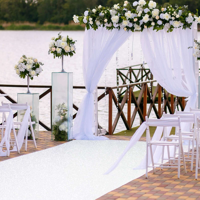 Elegant wedding ceremony setup by the water with floral arch and white chairs.