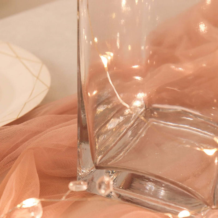 Clear glass vase on a soft pink fabric backdrop with fairy lights.
