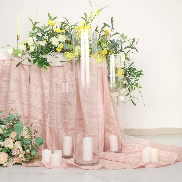 Elegant glass candle holders with white candles on a pink draped table.