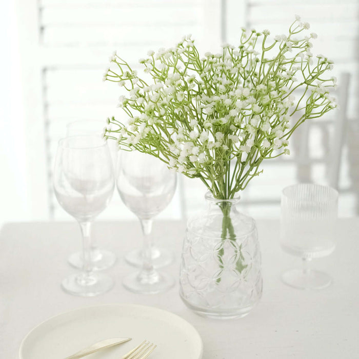Glass vase with white flowers next to elegant tableware and wine glasses.