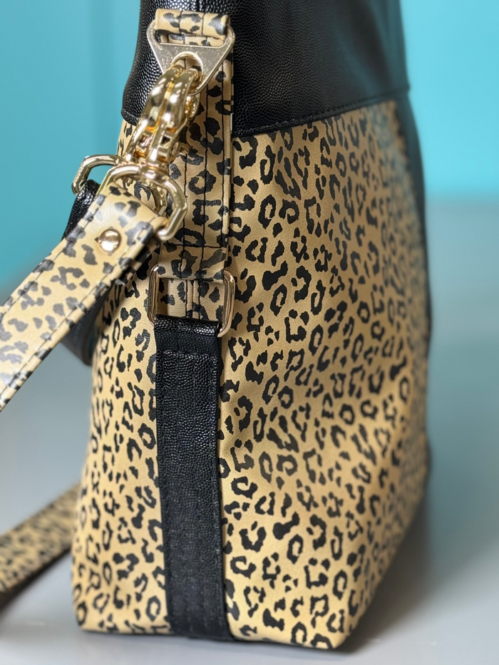 This shoulder bag is made with a textured black vinyl and a leopard print vinyl. It also has a matching crossbody strap. This photo shows the side of the bag.