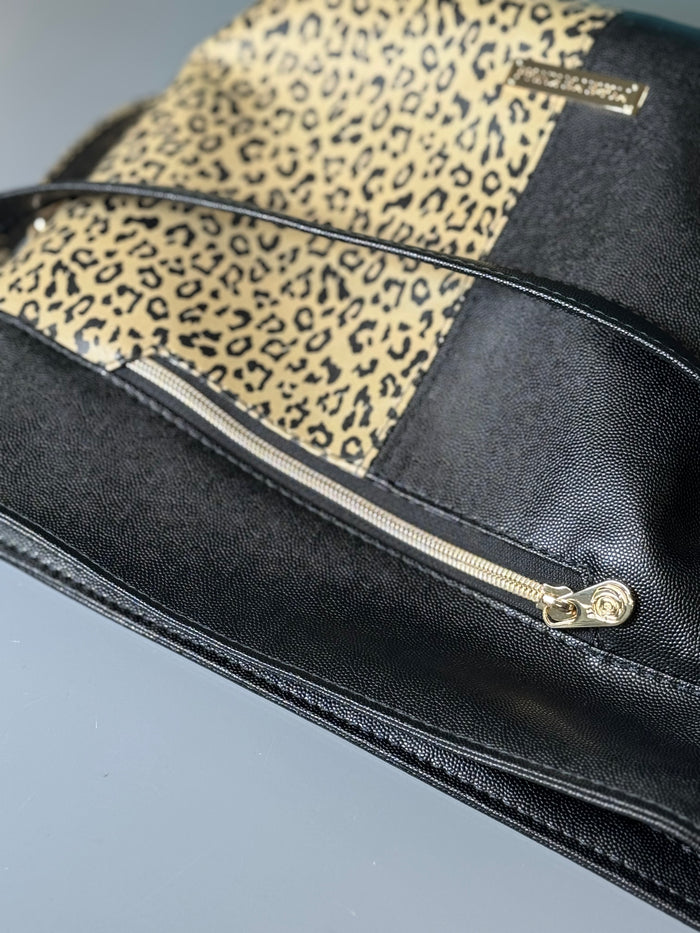 This shoulder bag is made with a textured black vinyl and a leopard print vinyl. This photo shows a close up of the exterior zipper pocket.