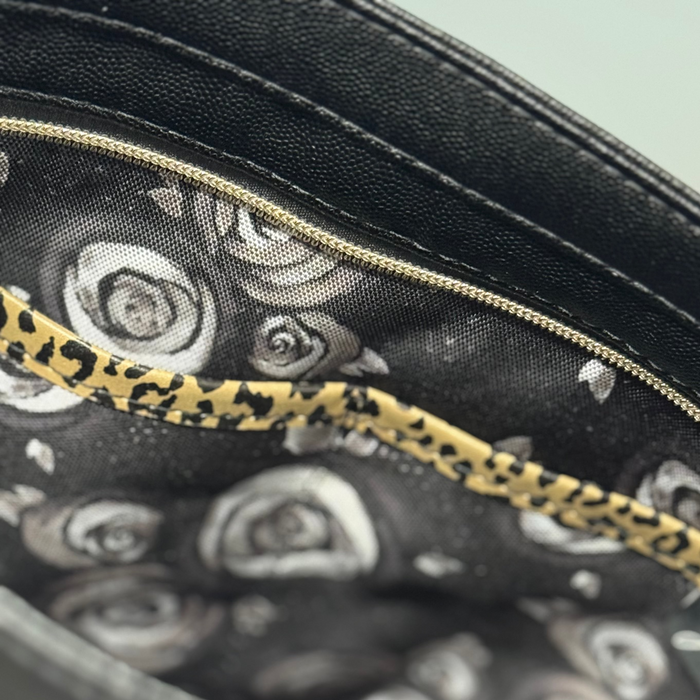 This shoulder bag is made with a textured black vinyl and a leopard print vinyl. This photo shows the inside of the bag with a black and white rose pattern fabric lining.