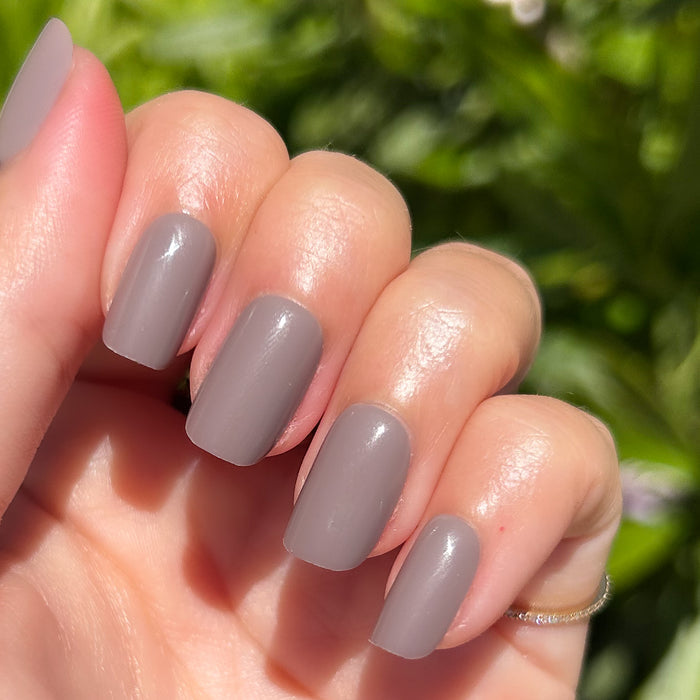 AW - Press-On | Short | Squoval showing hand with warm grey short squoval press-on manicure in natural sunlight outdoors