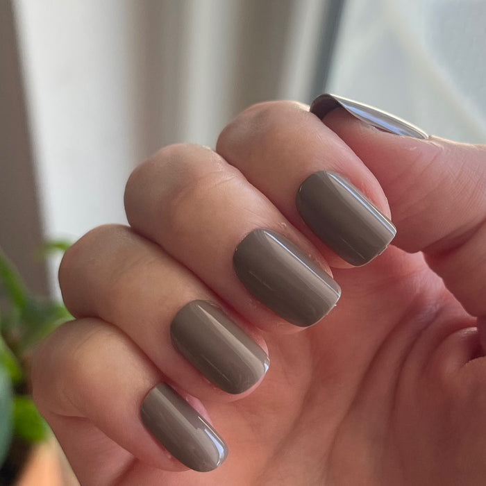 AW - Press-On | Short | Squoval showing hand with short squoval warm grey press-on manicure indoors near window light