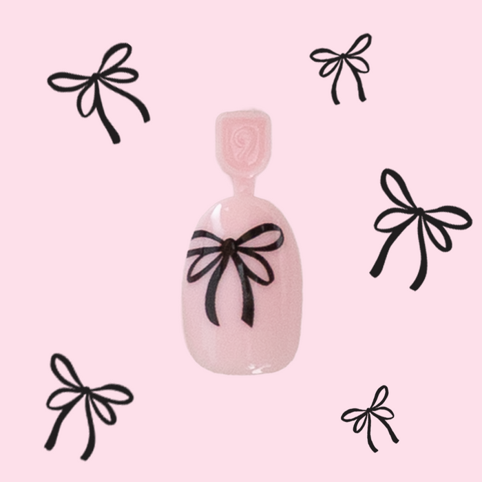 Biggest Bow On Top - Pressies | Short Medium | Round showing light pink press-on nail with black bow design on pink background