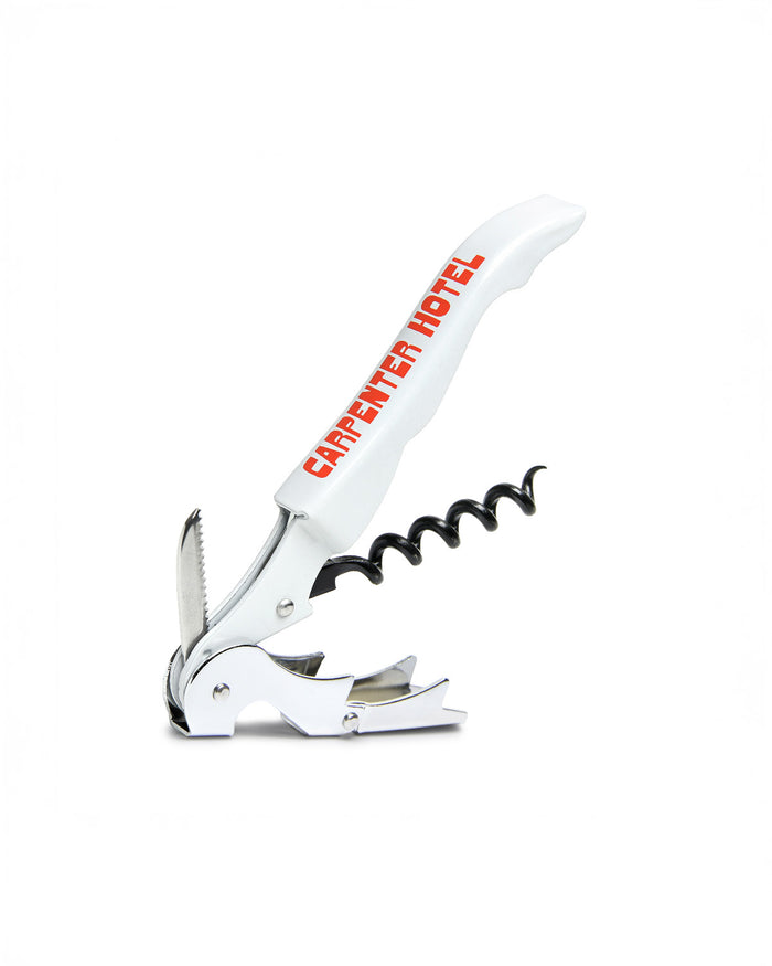 An open silver metal wine key with the Carpenter Hotel logo printed in orange-red on its side.