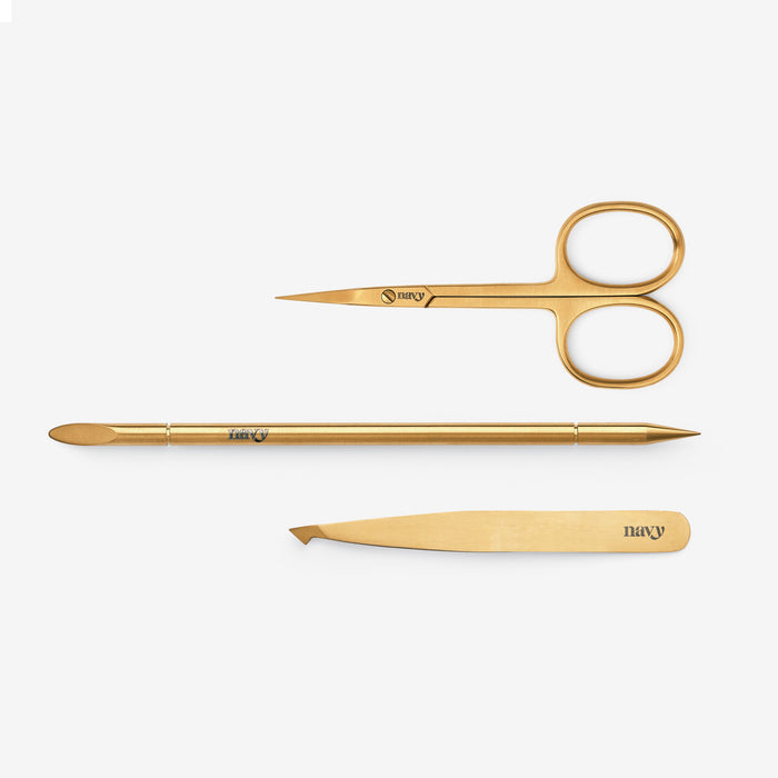 A collection of eyebrow grooming tools including a slant tweeze, straight scissor, and a reusable orange-wood stick.