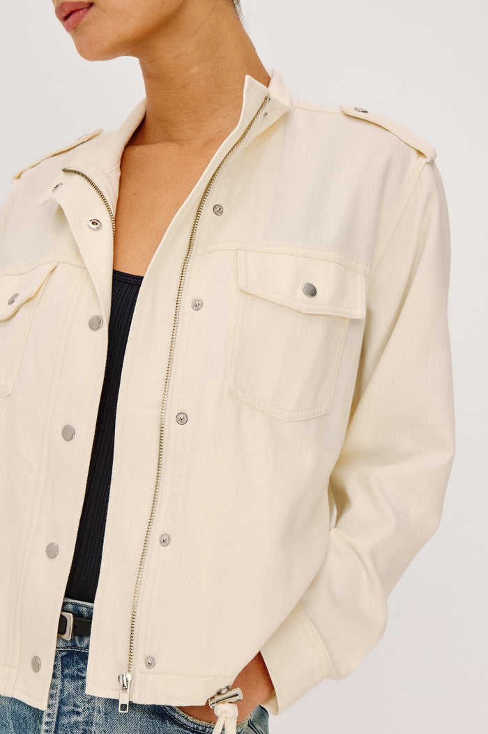 Collins Miitary Inspired Jacket With Shoulder Epaluettes, Stand Collar, Front Snap Buttons, Double Chest Pockets, Long Sleeves in Ivory Colorway - Upper Body Close Up Front View Featuered on Model