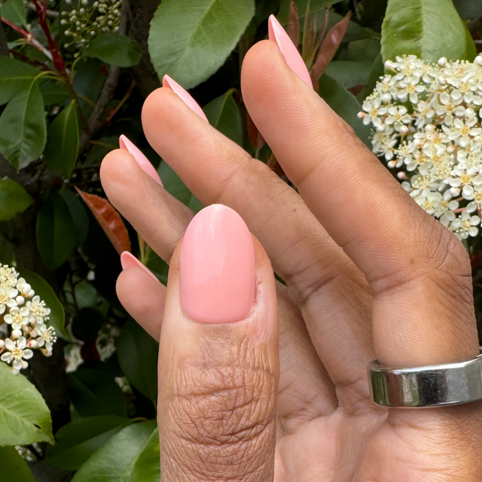 Creamsicle | Medium | Oval - Tab Press-On nails in glossy pastel coral pink on hand against green leafy and white floral background