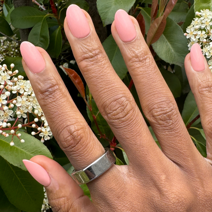 Creamsicle | Medium | Oval - Tab Press-On nails in soft pastel coral orange on hand with natural greenery and white flowers background