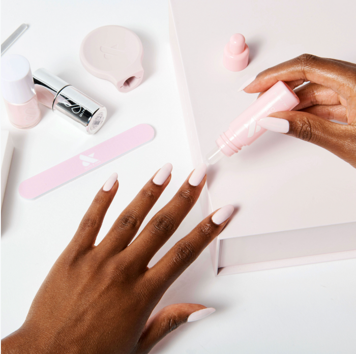 Hand with light pink nails applying Dry Drops for fast-drying manicure alongside nail care tools by Olive and June