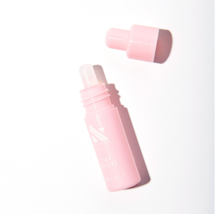 Pink bottle of Dry Drops with dropper cap removed on white surface for fast-dry mani care by Olive and June