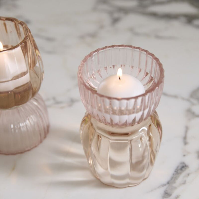 Two glass candle holders with a lit candle on a marble surface