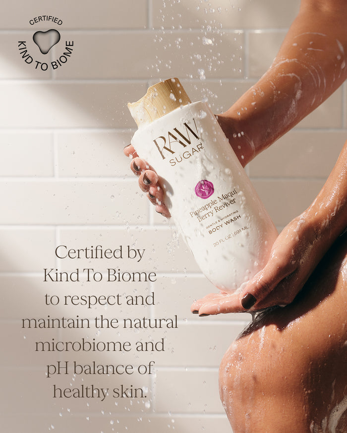 Person holding a bottle of Raw Sugar body wash in a shower setting, with text about certification by Kind To Biome.