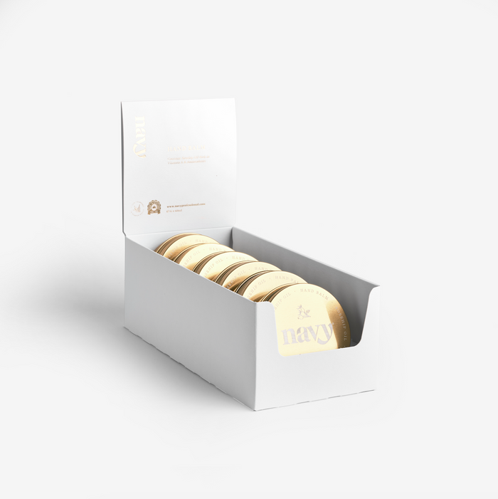 A white retail pack containing six gold-colored hand balm containers, displayed with an open lid and the brand name visible.