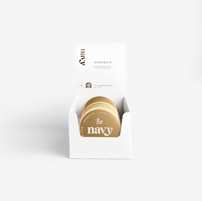 A white retail pack containing six gold-coloured hand balm containers, displayed with an open lid and the brand name visible.