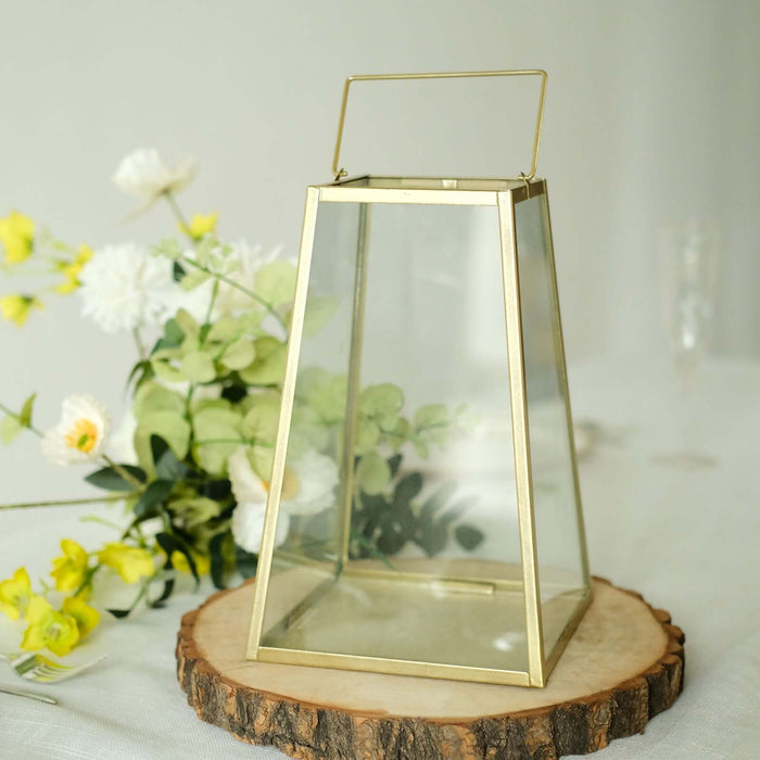 Glass lantern with gold frame and handle, surrounded by flowers.
