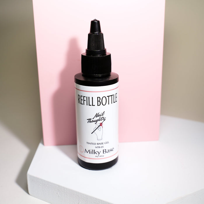 A bottle of Nail Thoughts Tinted Base Coat Milky Base gel positioned on a surface with a pink background.
