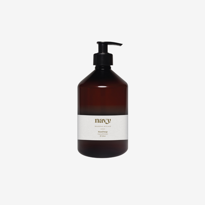 A dark amber glass pump bottle with a white label reading 'navy' and 'handmade soap', set against a plain light gray background.