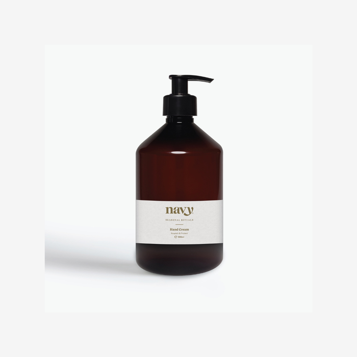 An amber glass pump bottle with a black dispenser and a white label reading 'navy' and 'Hand Cream' on a light gray background.