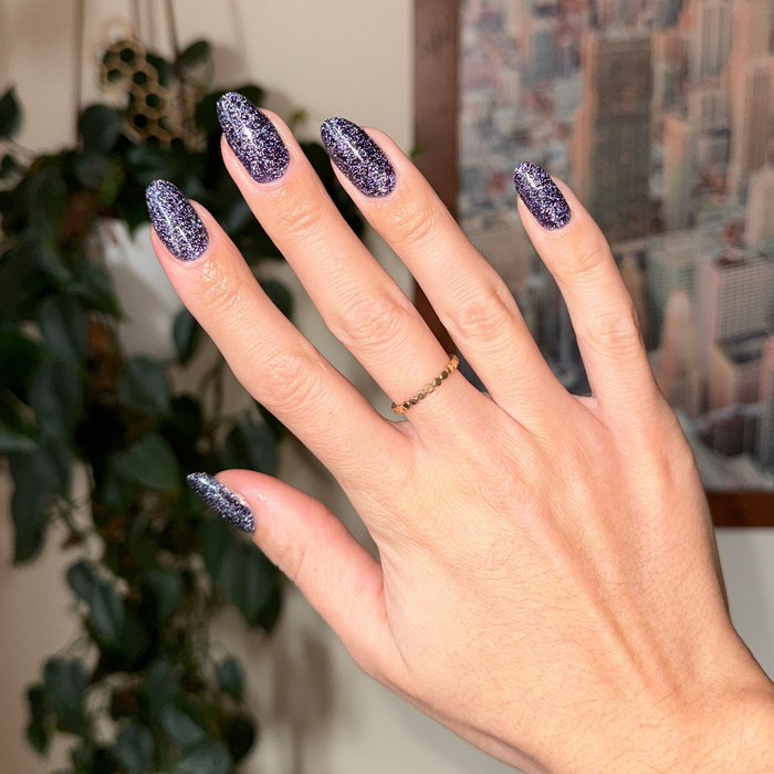 Hand with long nails painted in dark glittery gel polish from the Flash Glitter Set for a sparkling manicure look