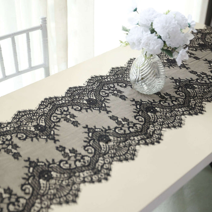 Black lace table runner on a beige table with a vase and flowers.