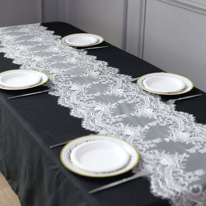 Lace table runner on a black table with white plates and silver cutlery.