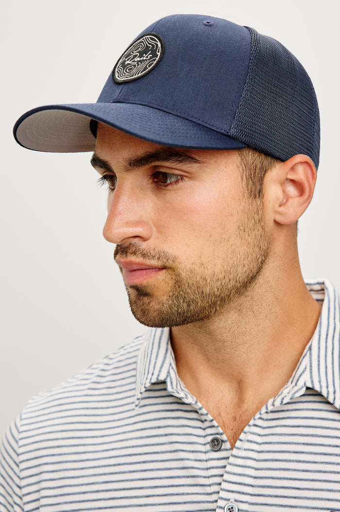 Golf Hat With Embroidered Branded Patch at Front, Adjustable Snapback, Mesh Back, and 6-Panel Construction in Navy Colorway - Upper Body Front View Featured on Model
