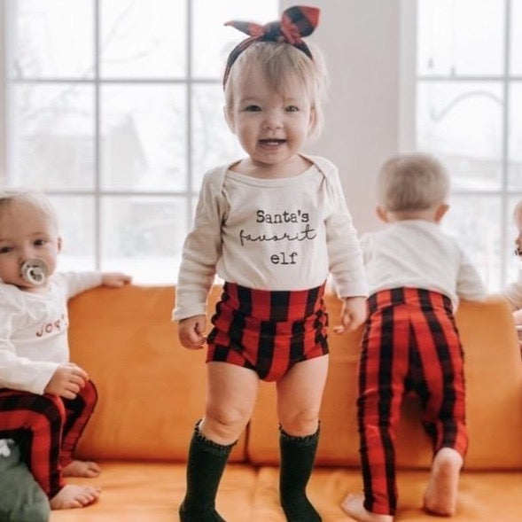 Baby wearing red buffalo plaid bummies and a matching headband, styled with a 'Santa's cutest elf' onesie. Perfect holiday outfit for babies and toddlers.