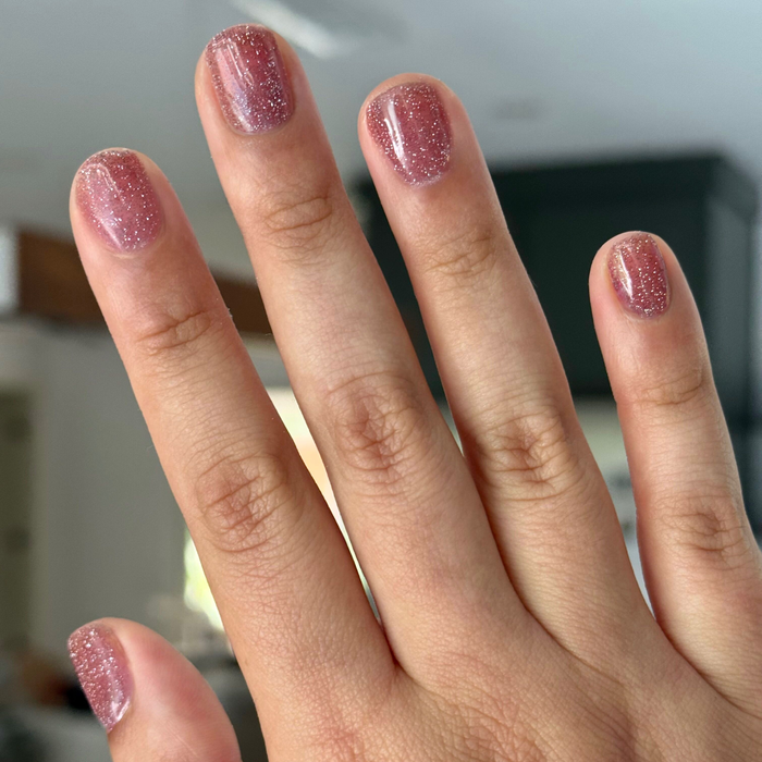 Hand with nails painted in Rosé Rhymes with Partay Gel showing sparkling cool-toned pink glitter manicure