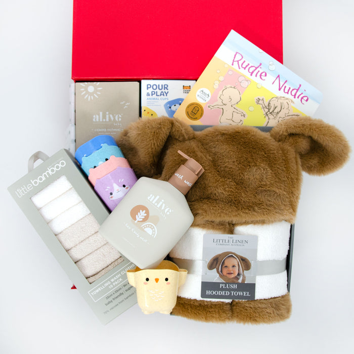 A baby gift hamper set including a plush hooded towel with puppy ears, organic hair and body wash, bamboo towelling washers, stacking animal cups, and a board book, all displayed in a red box. Price: 149
