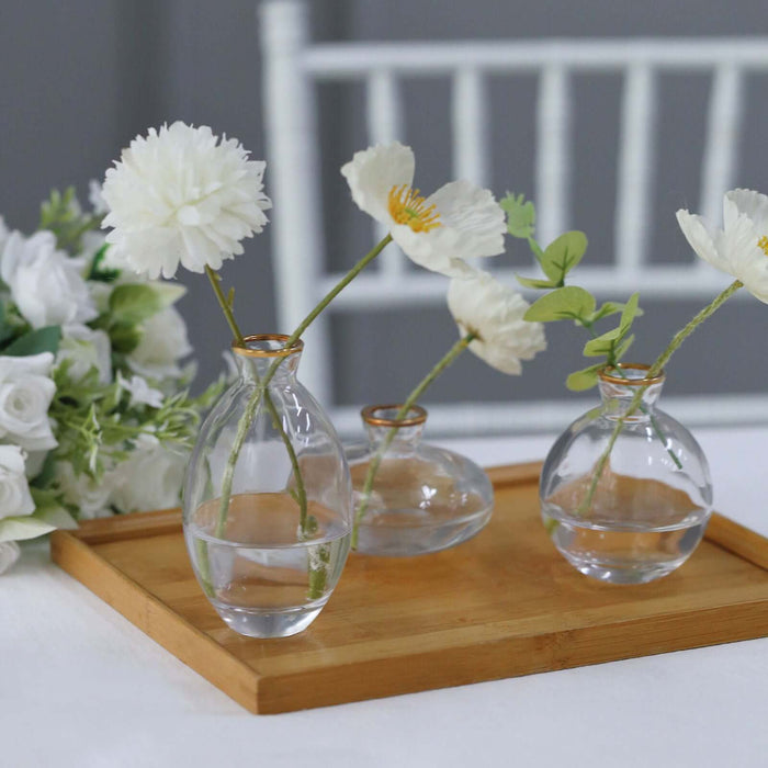 Clear glass vases with flowers on a wooden tray.