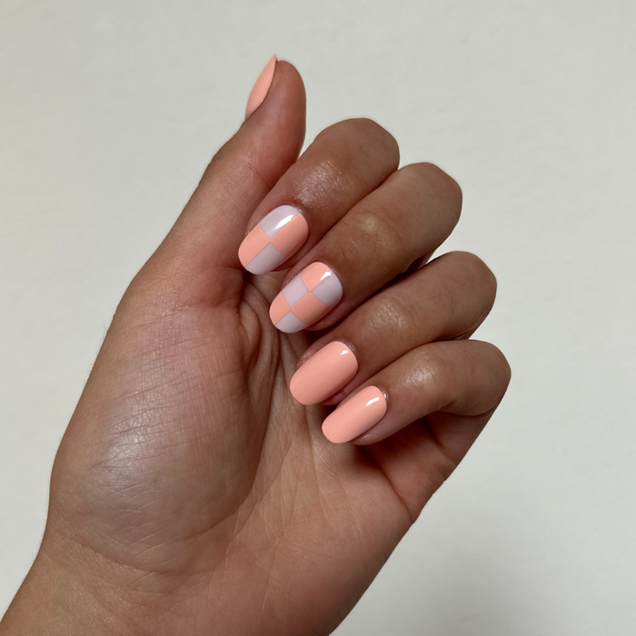 Sherbet Checker Party | Short | Round - Tab Press-On nails in peach and pastel pink checkerboard with solid peach nails on hand