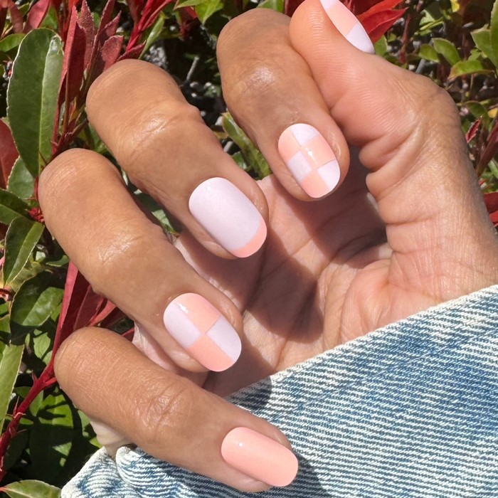 Sherbet Checker Party | Short | Round - Tab Press-On nails in pastel pink and peach with checkerboard and solid color design on hand