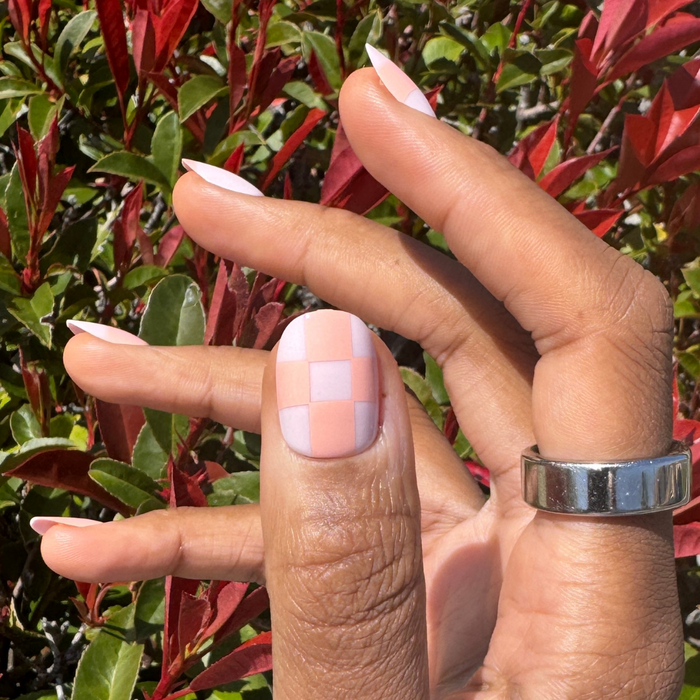Sherbet Checker Party | Short | Round - Tab Press-On nails in pastel peach and pink checkerboard on hand outdoors