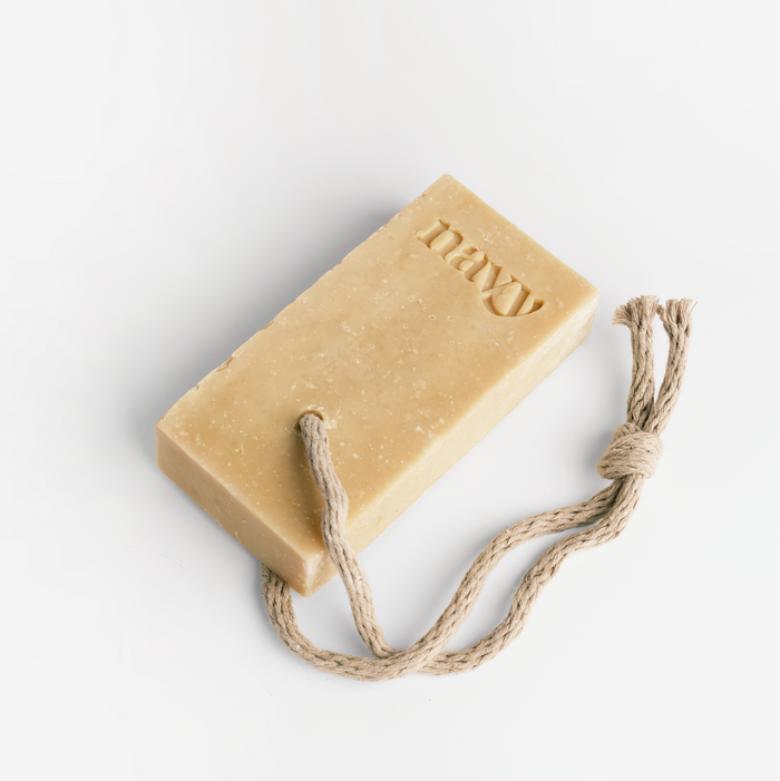 A beige bar of soap labeled 'NAVY' attached to a rope, set against a white background. Hint of Navy signature scent