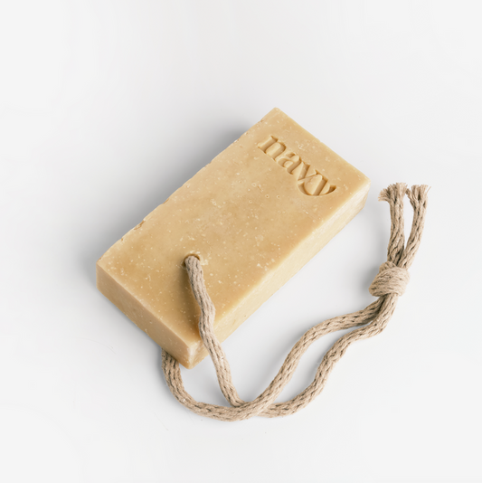 A beige bar of soap labeled 'NAVY' attached to a rope, set against a white background. Hint of Navy signature scent