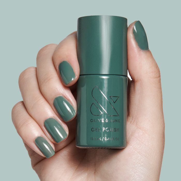 Hand holding Still Life of Flowers - Gel polish bottle with matching mossy green gel manicure on pale background