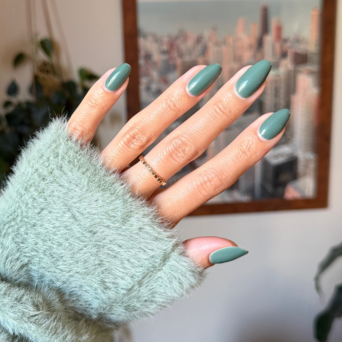 Hand with almond-shaped nails in Still Life of Flowers - Gel cool mossy green gel polish against blurred city background