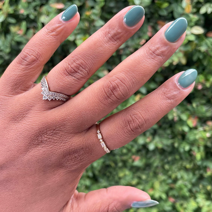 Hand with oval nails painted in Still Life of Flowers - Gel long-lasting mossy green gel polish against a natural leafy backdrop
