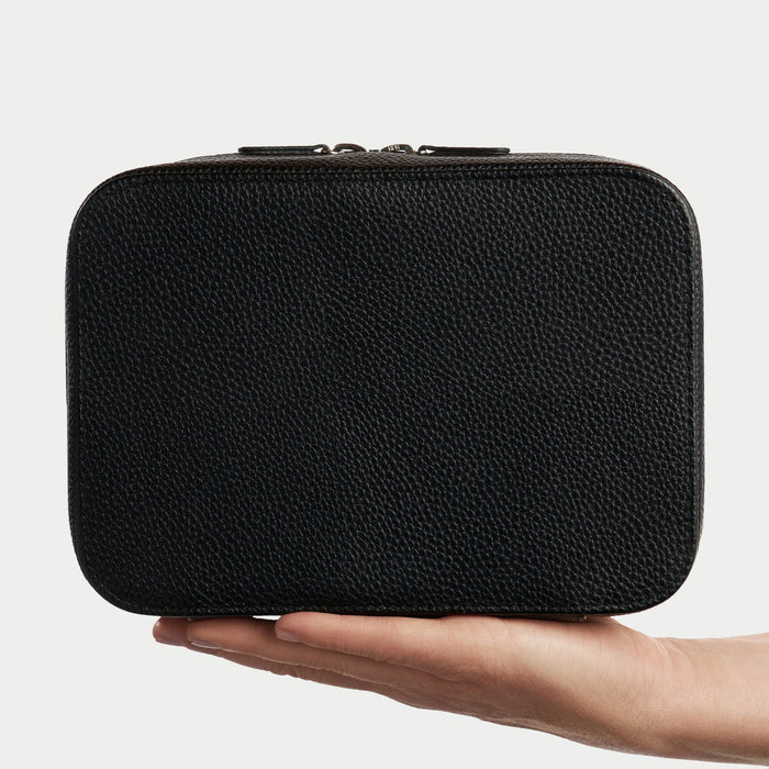 Black textured rectangular pouch held in a hand against a light gray background