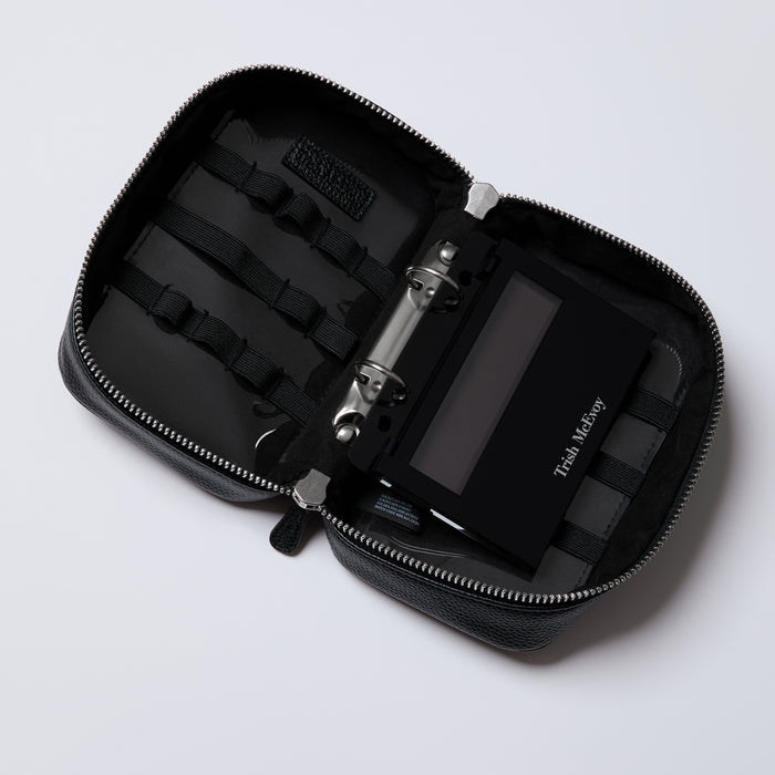 Black travel case with a phone and other items on a light gray background